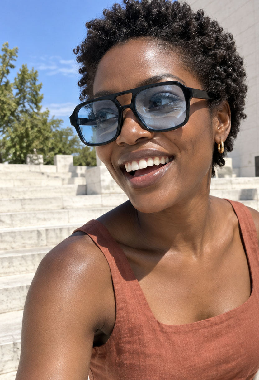 Smiling woman in a terracotta dress wearing NEW STATEMENT AZTEC sunglasses on stone steps outdoors #color_blue