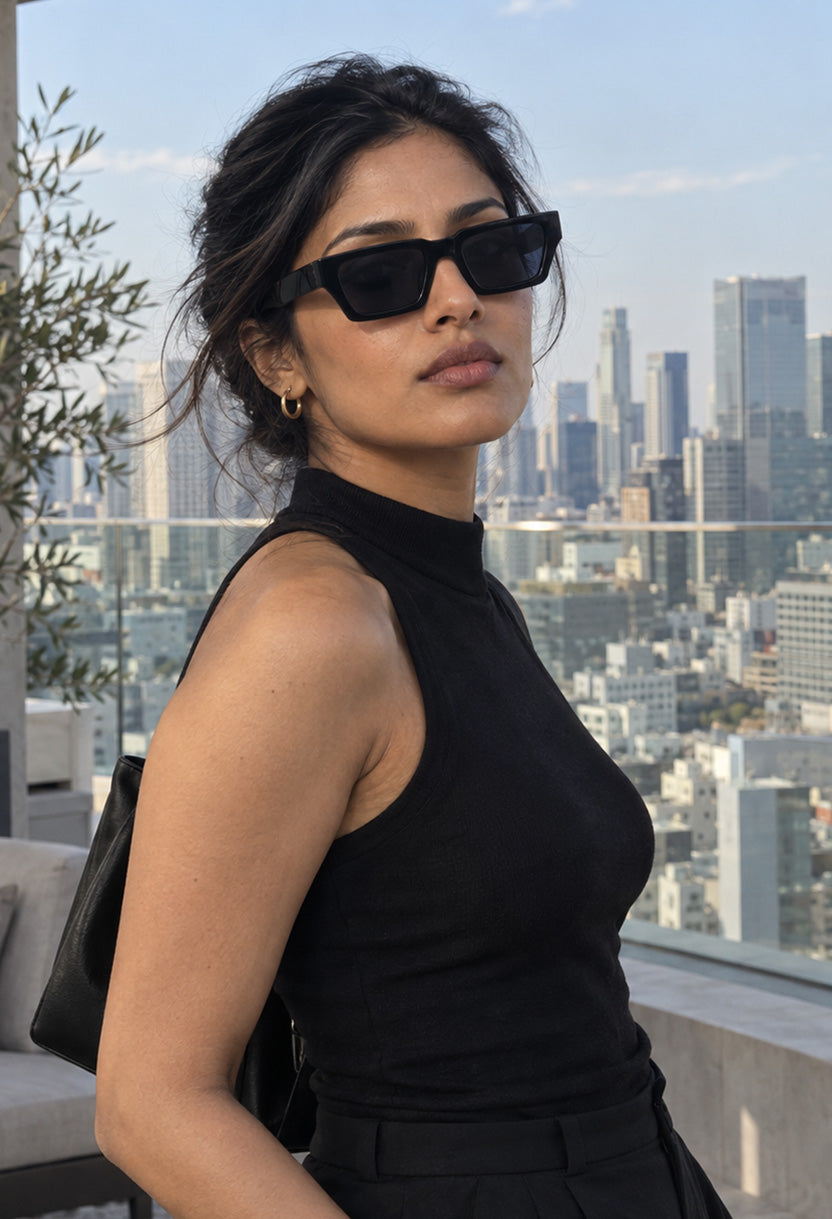 Woman in a black top wearing NEW STATEMENT NEXUS sunglasses in black on a rooftop with a city skyline #color_black