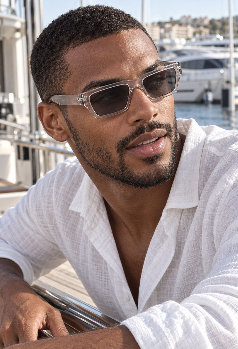 Man in a white linen shirt wearing NEW STATEMENT NEXUS sunglasses in transparent at a marina #color_transparant